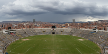Estadio Hernando Siles de La Paz desierto bajo un cielo tormentoso, con gradas vacías con los colores paceños.