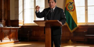 Presidente Rodrigo Paz en podio presidencial con bandera de Bolivia de fondo, hablando con ademán firme en discurso.