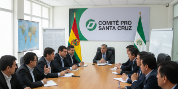 Símbolos cívicos de Santa Cruz y la bandera de Bolivia sobre una mesa de madera de una oficina directorio moderna.