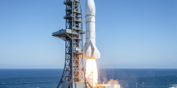 Un imponente cohete espacial metálico posado en una plataforma de lanzamiento costera bajo un cielo azul